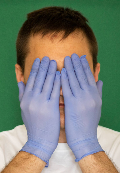 facet w rękawiczkach medycznych trzymając białą maskę medyczną na zielonym tle - Zdjęcie, obraz