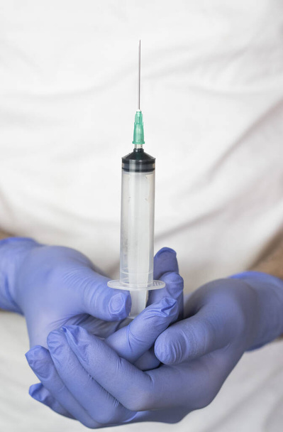 lékař v modrých lékařských rukavicích držící injekční stříkačku s jehlou detailní - Fotografie, Obrázek