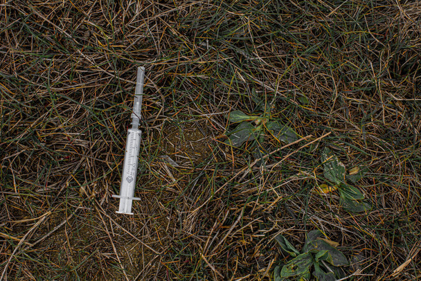 malá lékařsky bílá použitá injekční stříkačka leží na zelené tmavě vysoké trávě  - Fotografie, Obrázek