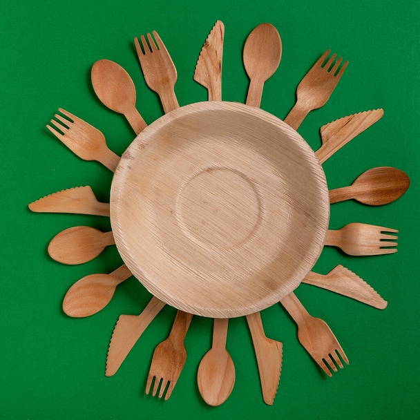 Eco-friendly disposable utensils made of bamboo wood on a green background. Draped spoons, fork, knives, bamboo bowls with. - Photo, Image