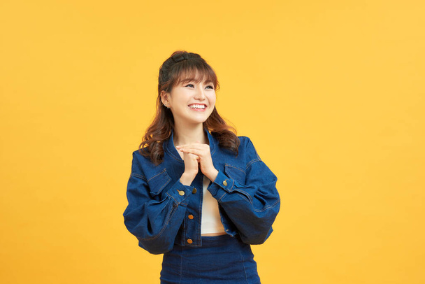 Close up photo of excited cheerful nice glad positive optimistic young lady holding hands together looking at you isolated yellow background - Photo, Image