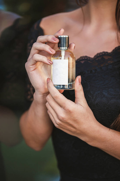 Perfume bottle of a female hand. Young stylish woman holding a bottle of perfume. Fashionable perfume in the hands of women. Girl spraying perfume. Beautiful female hands. Perfumes for women - Photo, image