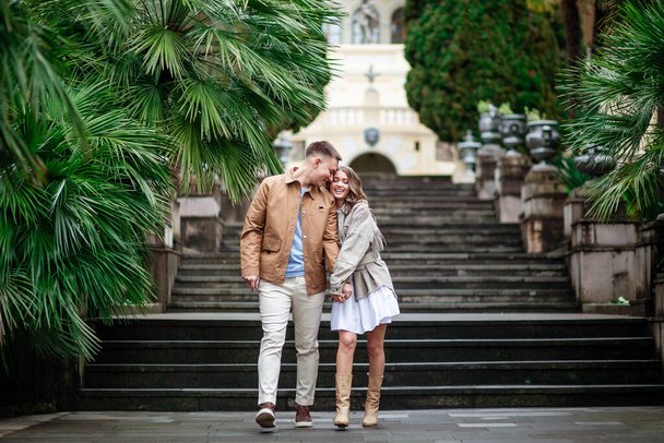 Счастливая влюбленная пара гуляет по парку под пальмами, держась за руки. Парень и девушка в отношениях
.  - Фото, изображение