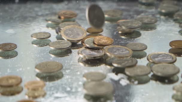 Plata y monedas de oro cayendo bajo el agua en cámara lenta y creando burbujas
 - Metraje, vídeo