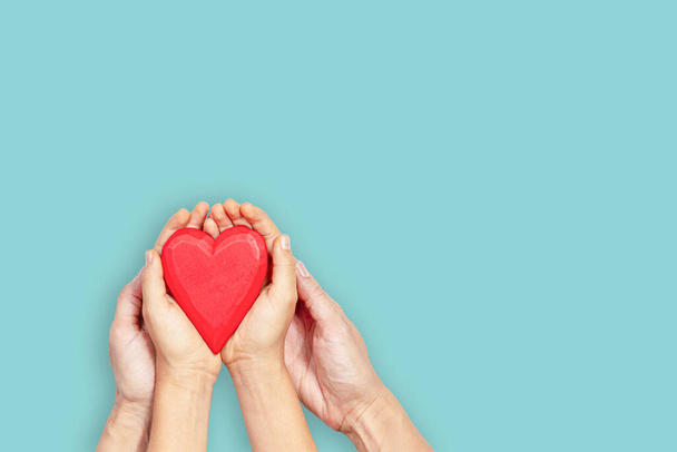 Volwassene en kind handen houden rood hart over witte achtergrond. Liefde, gezondheidszorg, familie, verzekering, donatie concept - Foto, afbeelding