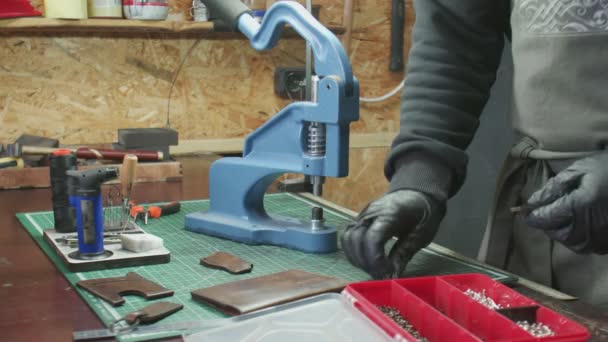 Close up de homem bronzeador em luvas pretas usa uma prensa para instalar acessórios de metal. Processo de trabalho na oficina de couro
. - Filmagem, Vídeo