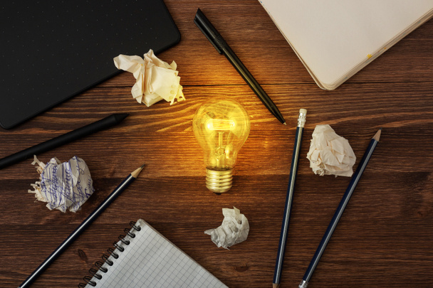 Creative idea inspiration concept by web designer or digital artist. New idea and Innovation with Crumpled Paper light bulb on brown wooden background. Pens, pencils, notebook, graphic tablet on table - Photo, Image