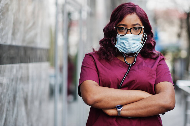 African american female doctor at red lab uniform in protective facial mask. Medicine, profession and healthcare concept. Stop coronavirus infection. - Fotoğraf, Görsel