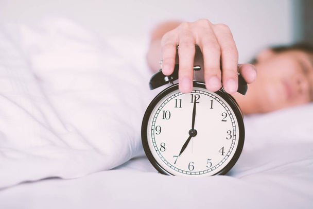 Γυναίκα κοιμάται στο κρεβάτι κλείνει το ξυπνητήρι ξυπνάει το πρωί, επιλεκτική εστίαση - Φωτογραφία, εικόνα
