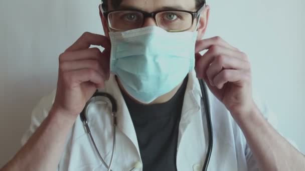 A young handsome doctor with glasses takes off his medical mask and sighs in relief. A young doctor takes off his protective mask and sighed with relief, rejoicing in the patient's recovery. - Filmagem, Vídeo