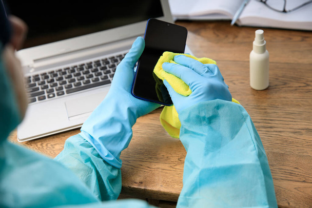 Limpieza en casa, en la oficina rociando una botella de desinfectante antibacteriano contra el coronavirus, manos en guantes azules. Descontaminación hospitalaria, prevención del espacio de oficinas. Superficie de desinfección antes de la explosión de COVID-19
 - Foto, imagen