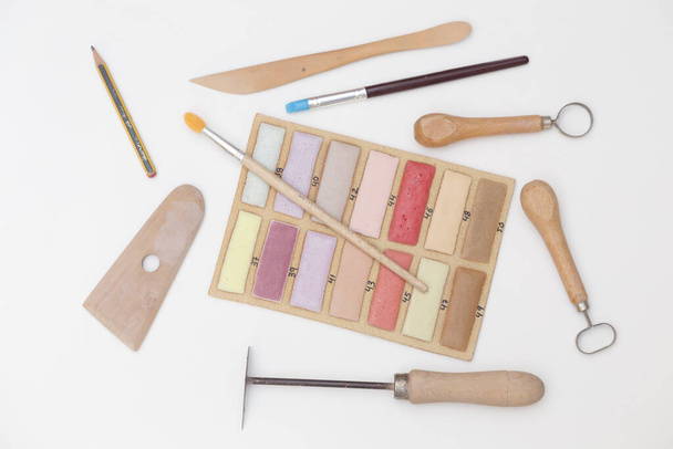conjunto de herramientas de modelado para cerámica, cortadores, palillo, paleta y una muestra de esmaltes, sobre fondo blanco
 - Foto, imagen