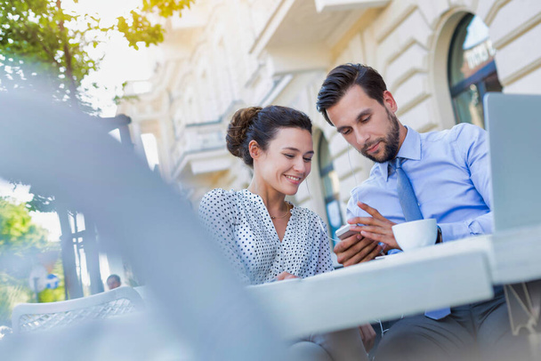 Businessman showing smartphone to businesswoman while having coffee during office break - Φωτογραφία, εικόνα
