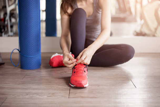 Pretty young sport woman is tying her sneakers in gym, Healthy lifestyle  - 写真・画像