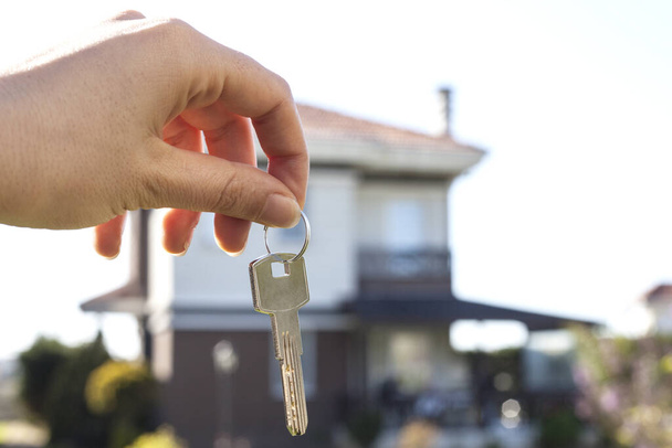 Κρατώντας τα κλειδιά του σπιτιού σε σχήμα σπιτιού μπρελόκ μπροστά από ένα νέο σπίτι - Φωτογραφία, εικόνα
