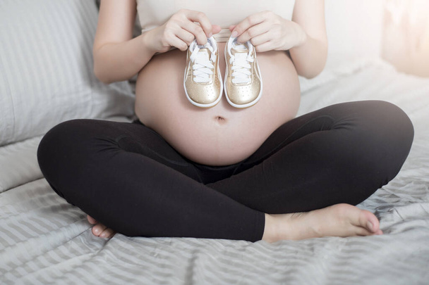 Güzel Asyalı hamile kadın küçük ayakkabılı bebeğini bekliyor. - Fotoğraf, Görsel