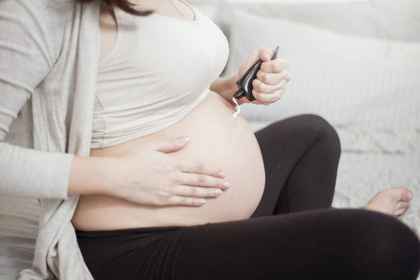 Primer plano de la mujer embarazada aplicando crema en su vientre
 - Foto, imagen
