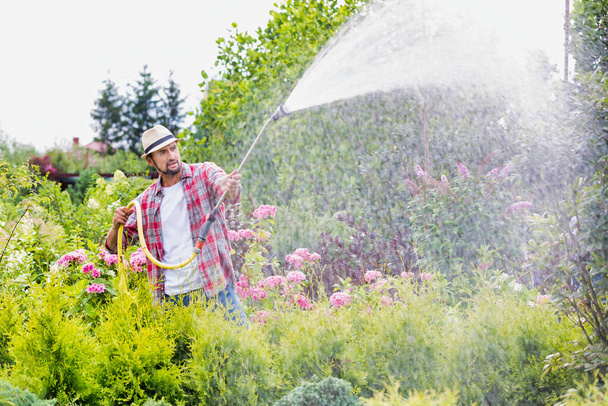 Photo of male gardener watering plants in garden shop - Foto, afbeelding