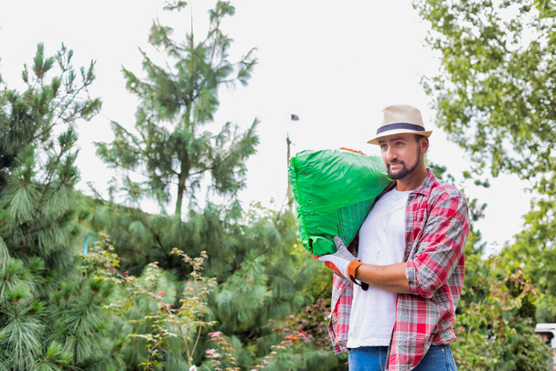 Portrait of male gardener carrying sack of soil on his shoulder while walking in garden shop - Fotó, kép