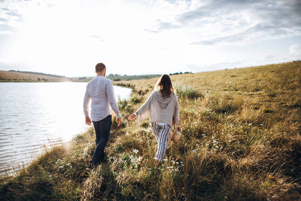 Beautiful loving couple walking on the shore, hugging, smiling on the sky background in the field. The guy and the girl hipster travel - Foto, Imagen