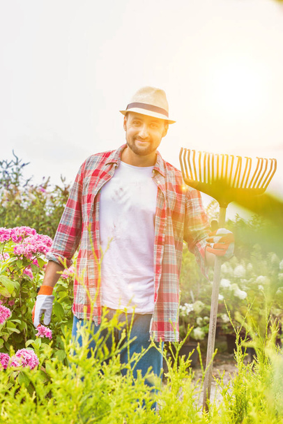 Portrait of mature gardener standing while holding fork rake - Foto, Imagem