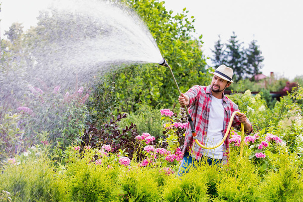 Portrait of mature gardener watering plants using hose in shop - Foto, Imagem