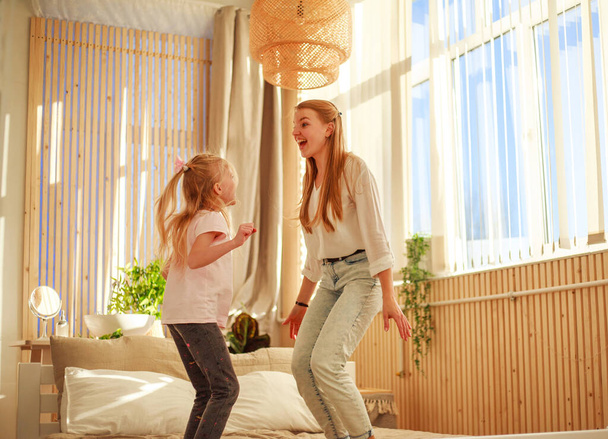 Mother and daughter on the bed at home jump, have fun, do acrobatic exercises, healthy leisure activity - Foto, immagini