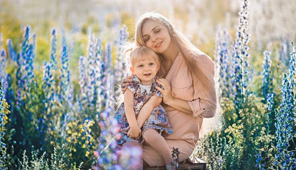 Beautiful blond woman with long hair with her little daughter in a flowering field - Фото, изображение