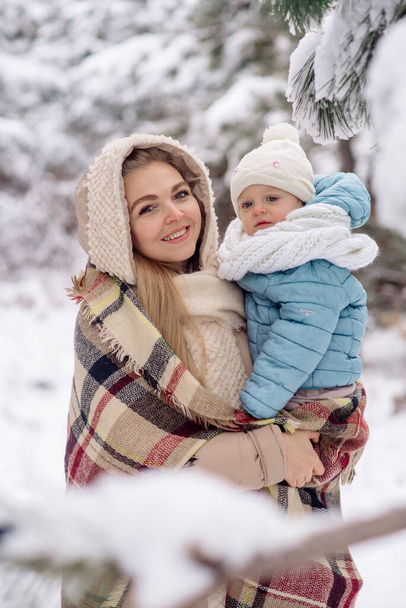 Mom holds in her arms a little daughter for a walk in the winter forest - Foto, Imagen