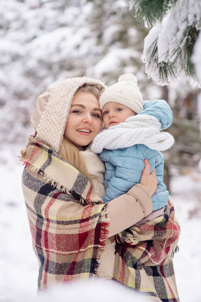 Mom holds in her arms a little daughter for a walk in the winter forest - Foto, Imagen