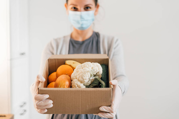 Young woman with face mask and gloves. Delivery fresh products to home. Covid-19 quarantine shopping - Photo, Image