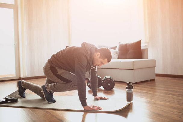 Young ordinary man go in for sport at home. Picture of real ordinary man doing abs exercising by running on one place with legs. Worksout freshman warming up body. Stretching alone in sunny apartment. - Photo, Image