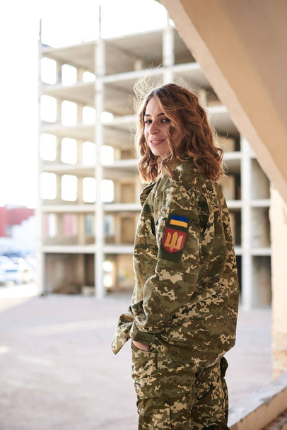 Young curly blond military woman,wearing ukrainian army uniform and black t-shirt. Three-quarter portrait of female soldier inside abandoned building. - Фото, зображення