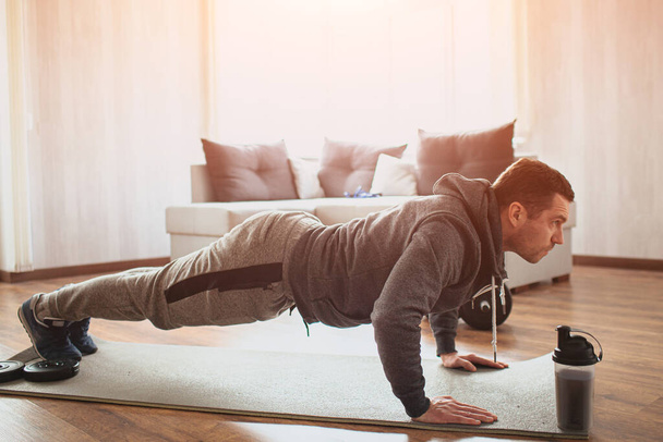 Young ordinary man go in for sport at home. Beginner freshman in exercising guy stand in plank position and look forward. Real picture of patient man working on his body shape. Start improve himself. - Photo, Image
