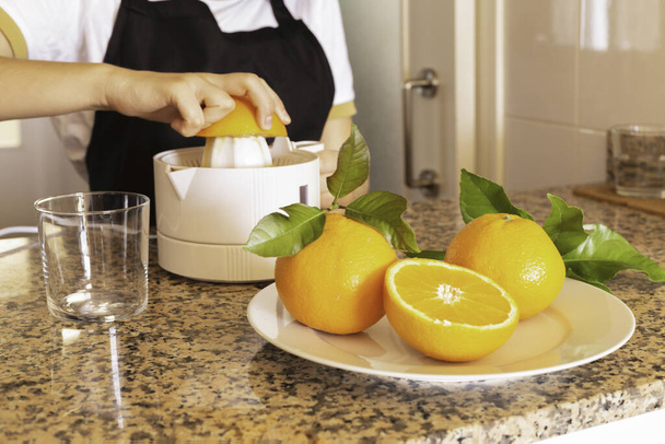 tiener meisje met een citrus sapcentrifuge met sinaasappel en verse citrusvruchten in de keuken - Foto, afbeelding