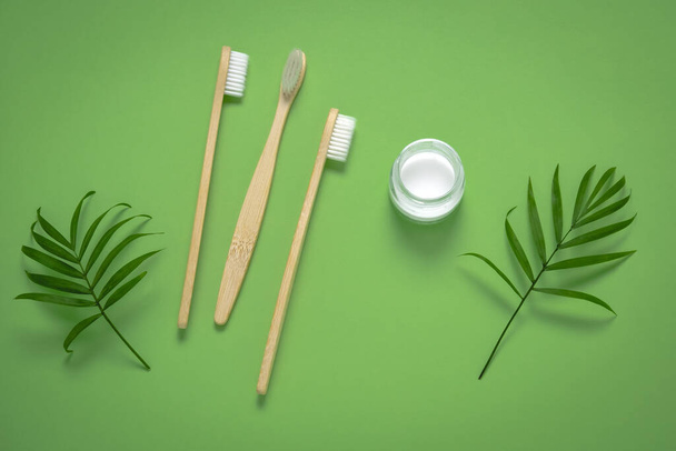 top view bamboo eco friendly tooth brushes, tooth paste jar and green tropical leaves, homemade toothpaste and dental care concept - Фото, зображення