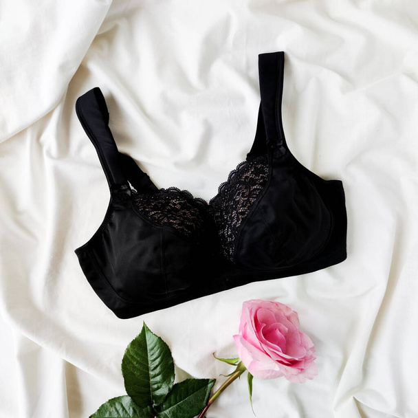 zwarte beha met zwart kant op een wit laken met een roze roos. plat lay, top view concept van mode sexy lingerie. - Foto, afbeelding
