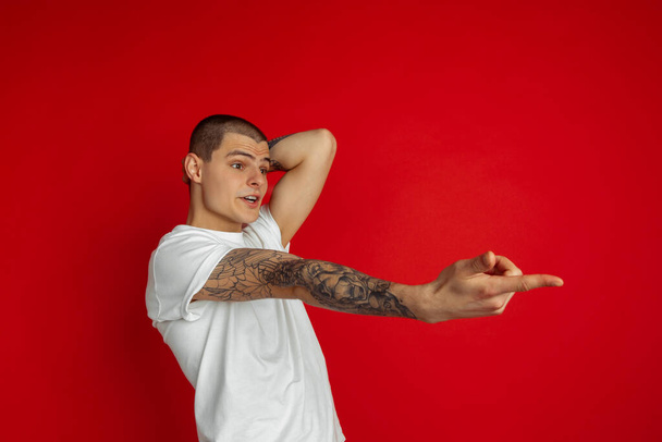 Caucasian young mans portrait on red studio background, emotinal and expressive - Фото, зображення