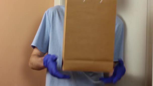 Een man met een masker en handschoenen geeft het pakket door aan degenen die het nodig hebben. Donatie. Sociale hulp. Quarantaine. - Video