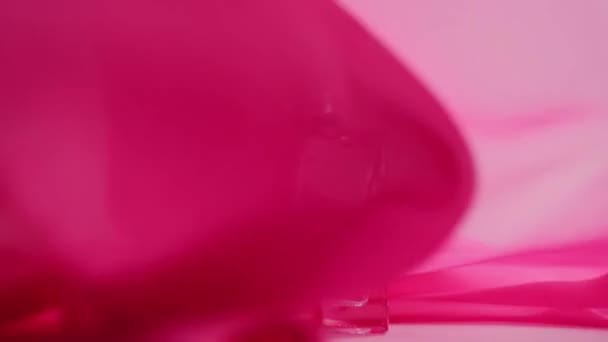 Flache Parfümflaschen mit Cyanparfüm oder ätherischen Ölen liegen auf dem Tisch. Pinkfarbener Stoff flattert herum und weht in der Luft um die Parfümflasche. Konzept von Aroma und Geruch. Nahaufnahme - Filmmaterial, Video