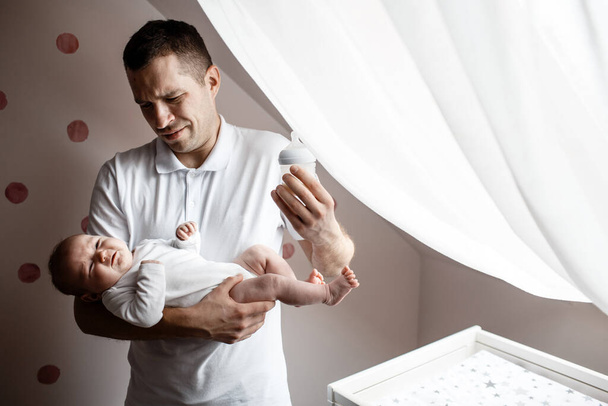 Father and little kid in the nursery. The first year of life. Uncertainty and fear of a child. Daddy does not know what to do with the child - Photo, Image
