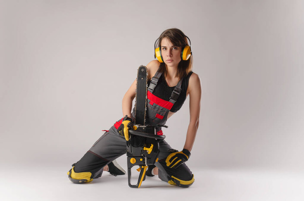 Girl in overalls with a chainsaw in white background - Photo, Image