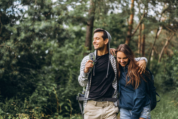 Young couple with backpacks on their backs smiling and walking in the forest, enjoy the walk. - Fotoğraf, Görsel