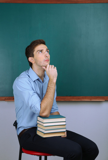 Young teacher sitting near chalkboard in school classroom - Foto, Imagen