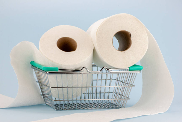 Toilettenpapierrolle in einem Miniatur-Einkaufswagen auf blauem Hintergrund. Konzept des Hortens und der Panik beim Kauf von Toilettenpapier während der Covid-19-Pandemie. - Foto, Bild