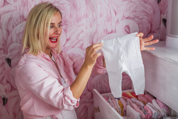 pregnant woman preparing wardrobe clothes for new baby - Foto, afbeelding