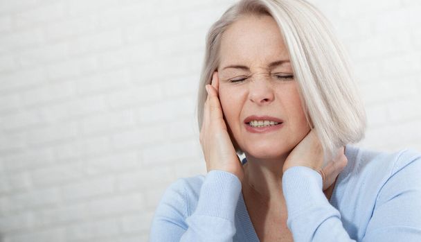 Kobieta cierpiąca na stres lub ból głowy grymaszący w bólu, gdy trzyma plecy szyi drugą ręką do skroni, z przestrzenią do kopiowania. Koncepcja zdjęcia ze wskazaniem miejsca bólu. - Zdjęcie, obraz