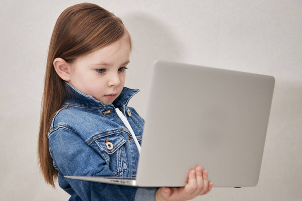 Portrait of a little girl holding laptop computer while standing - 写真・画像