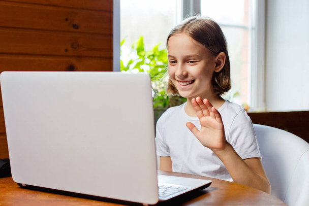 Enseñanza en casa. Una chica está sentada en una mesa con una computadora portátil durante un video chat en línea de una lección de la escuela con un maestro y una clase. Concepto de educación a distancia. Autoaislamiento en cuarentena
 - Foto, Imagen