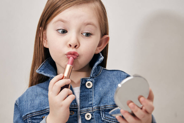 Little girl puts lipstick on her lips at home - Foto, imagen
